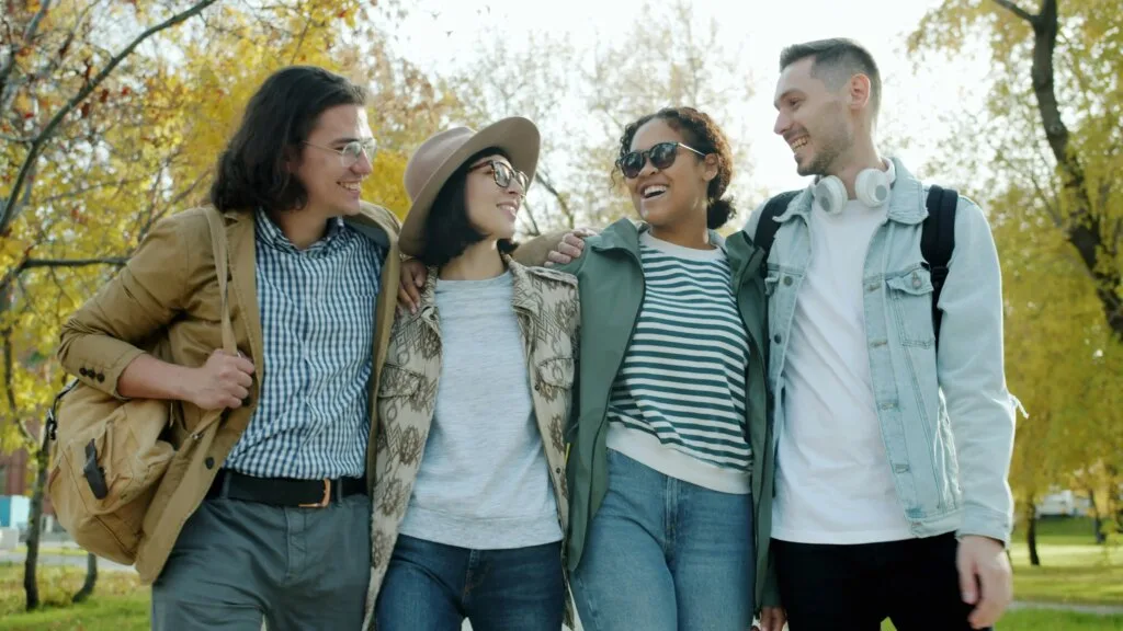 A diverse group of four friends laughing and walking together outdoors in an autumn park — representing real-world connection fostered through mindful social media use.
