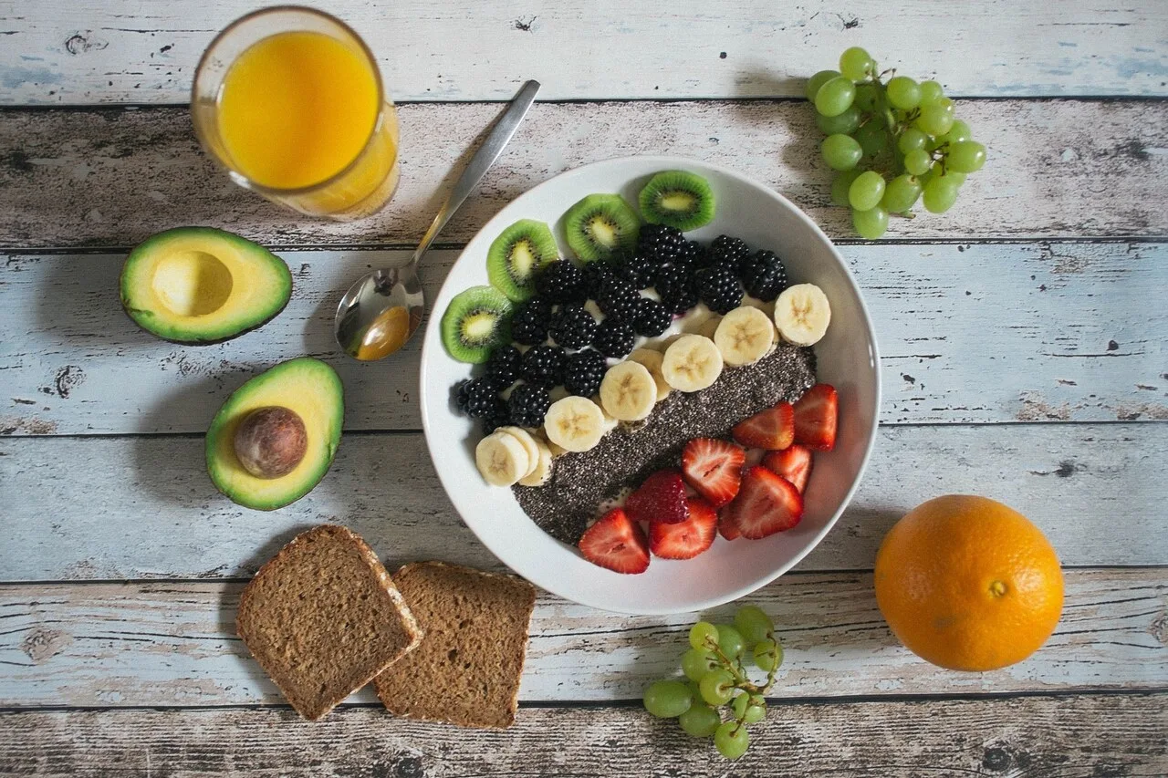 A bowl of high-fiber foods including berries, banana, chia seeds and kiwi surrounded by avocado, whole grain bread and fresh fruit