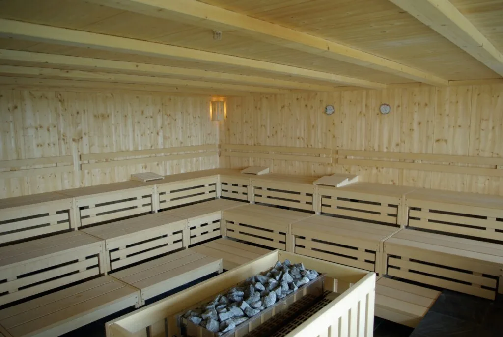 Interior of a large Finnish sauna with wooden benches and a traditional stone heater — a key recovery amenity offered by premium fitness and wellness clubs.
