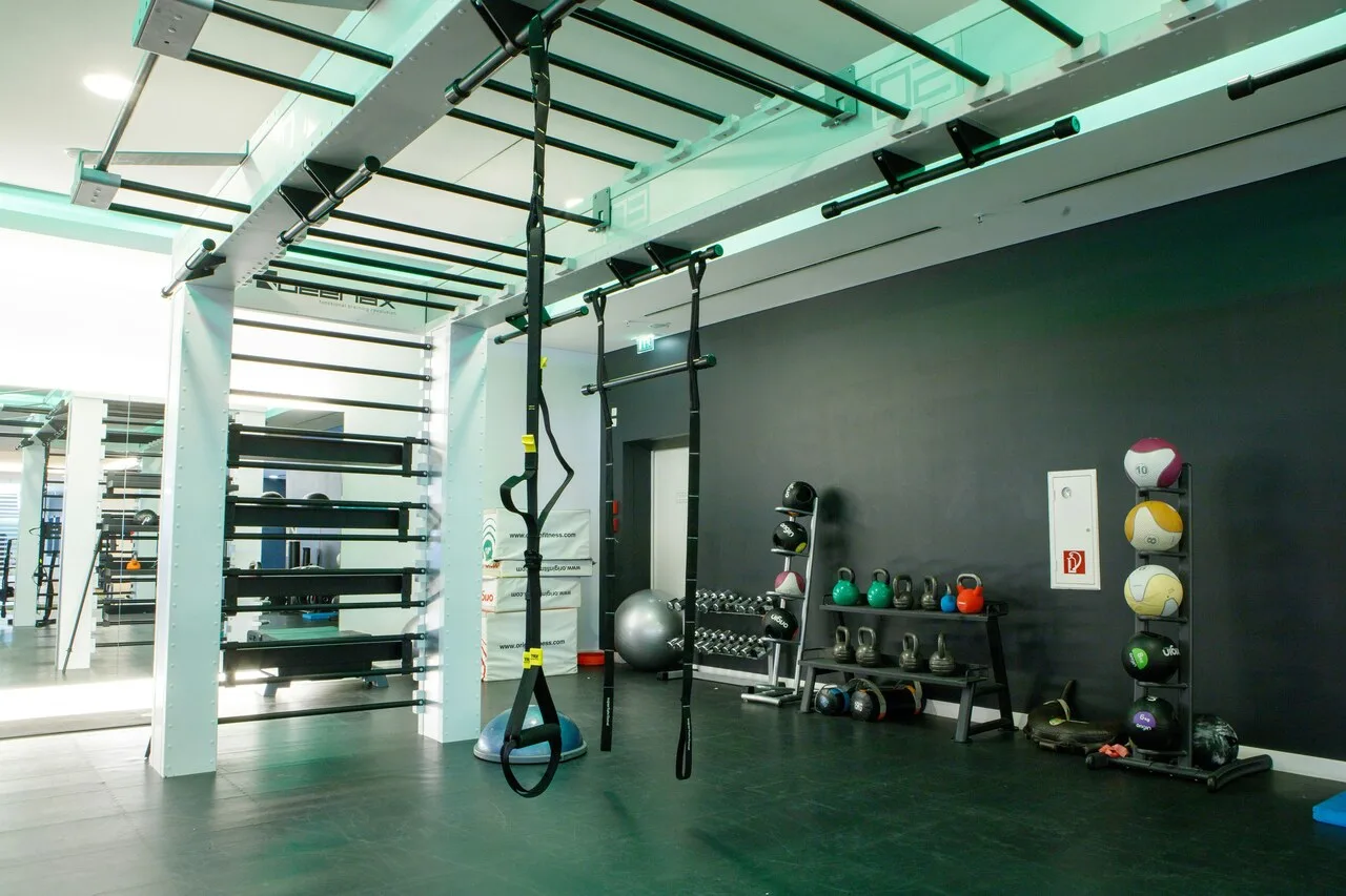 A modern premium fitness club interior featuring TRX straps, kettlebells, medicine balls, and wall bars — representing advanced training equipment for muscle health and longevity.