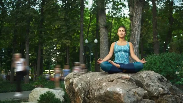 Woman meditating outdoors on rock representing present-moment awareness and mindfulness practice