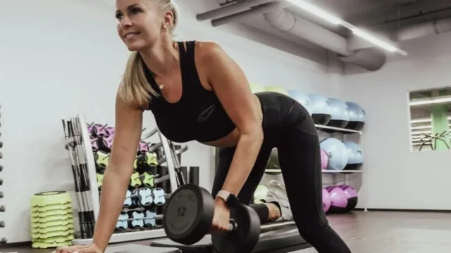 Woman doing dumbbell row strength training exercise in gym