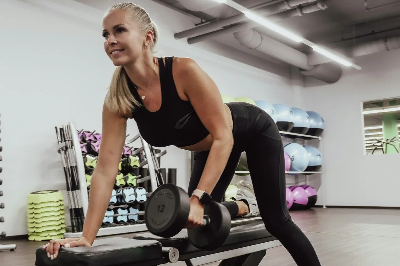 Woman doing dumbbell row strength training exercise in gym
