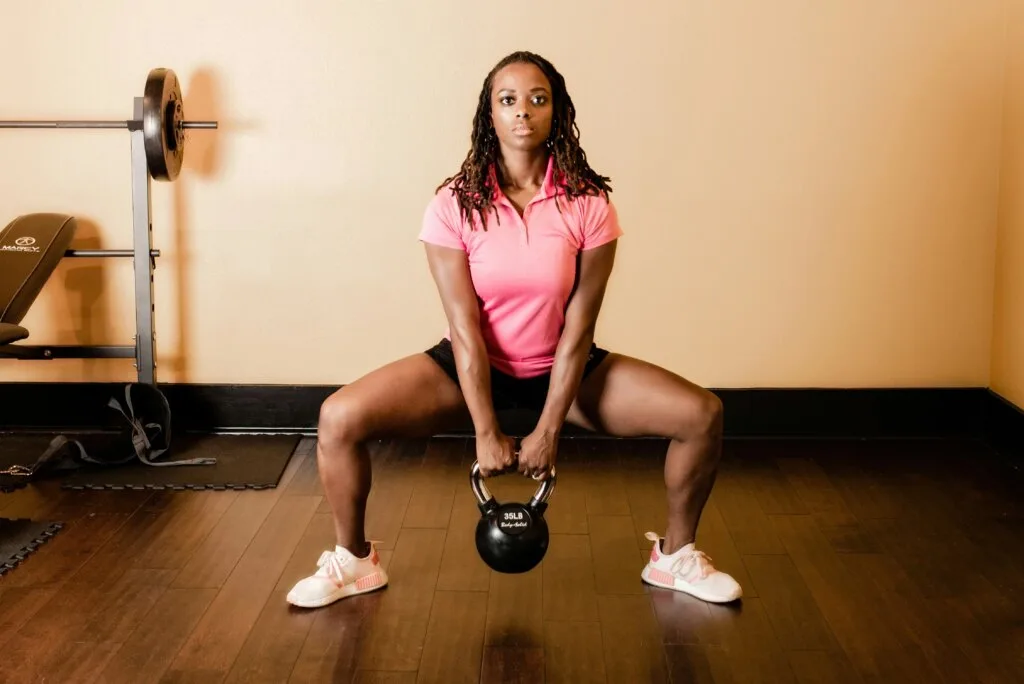 A woman performing a kettlebell squat during a strength training session in a gym — illustrating the importance of resistance training for muscle health and longevity.