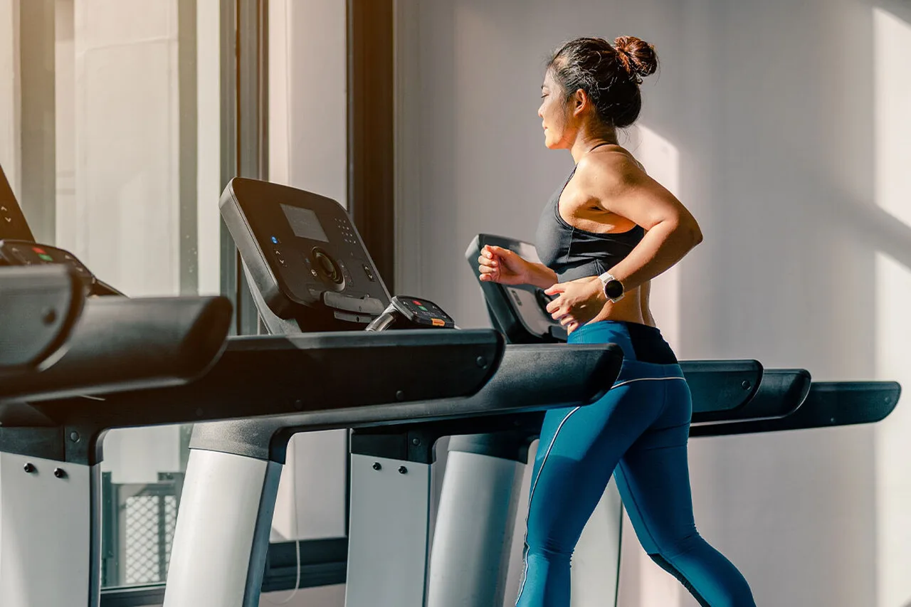 Woman running on a treadmill in a bright gym during a cardio workout