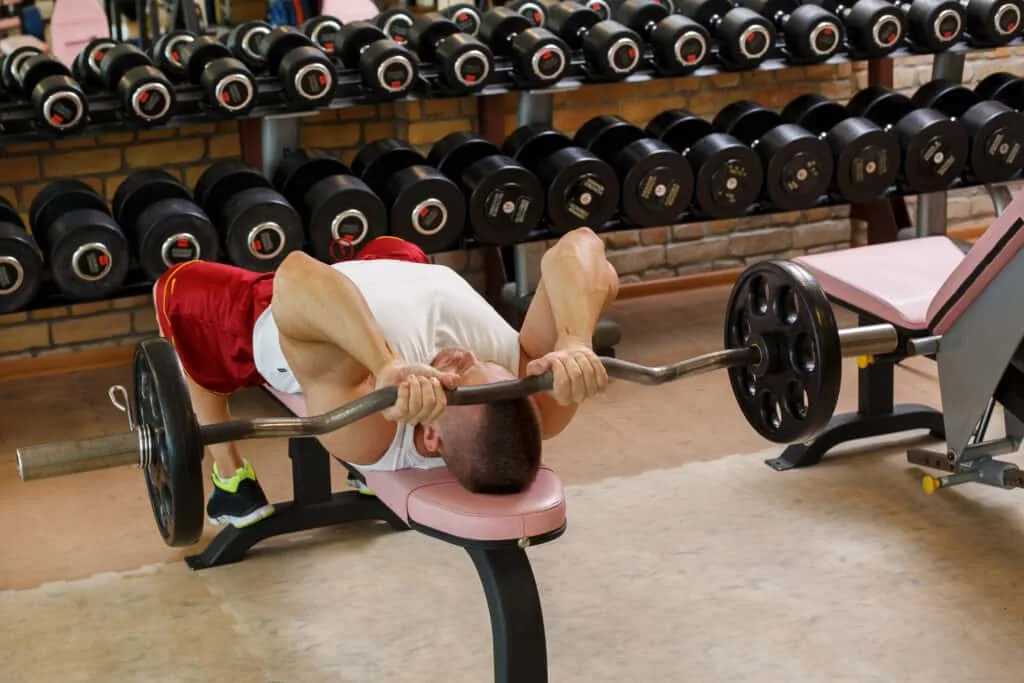 Man performing barbell triceps press on bench representing JM press technique for bigger stronger triceps