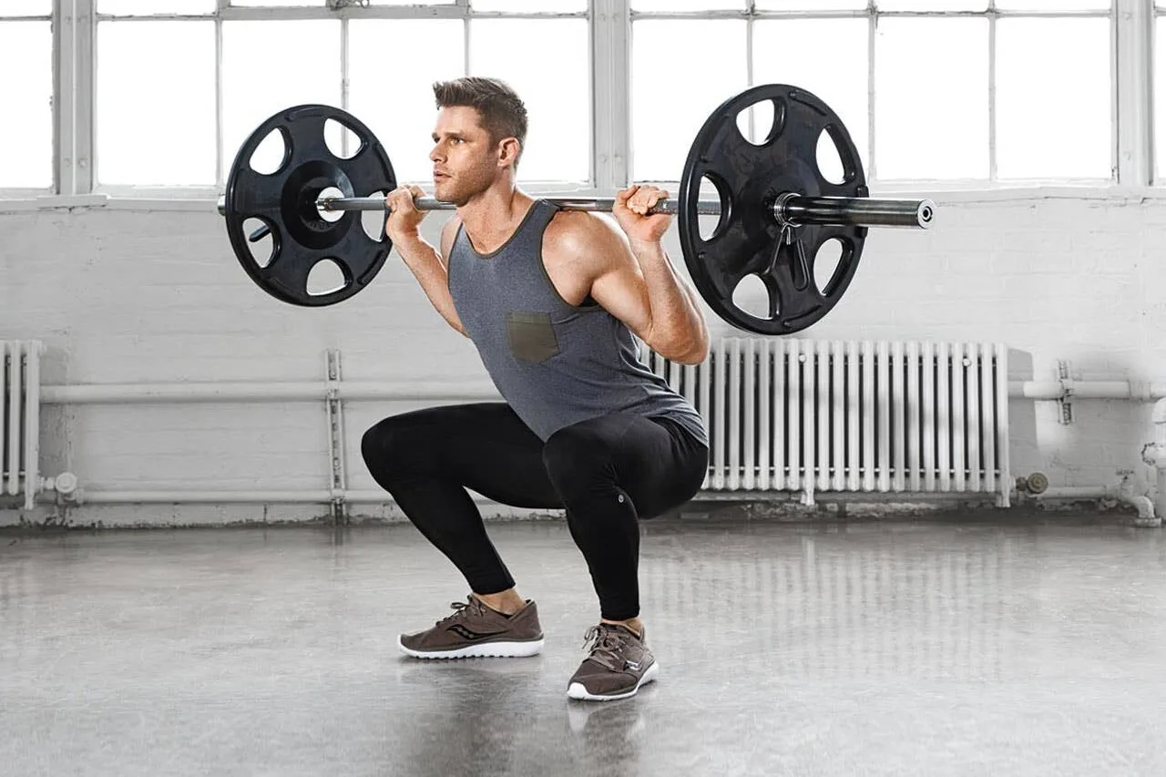 A man performing a barbell back squat in a bright gym studio — illustrating compound strength training essential for building a lean, ripped physique and optimal athletic performance.