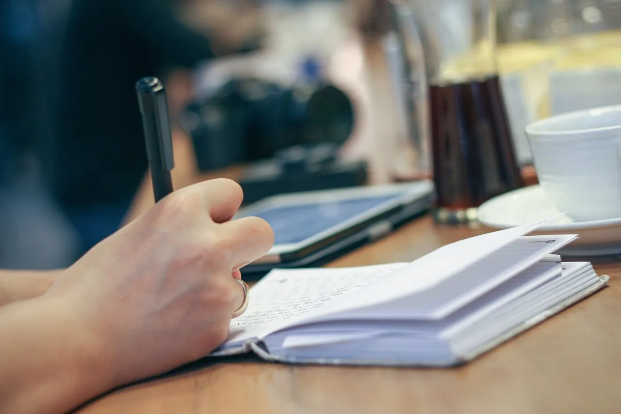 A close-up of a hand writing in a notebook with a pen, representing journaling as a mindfulness and self-reflection practice for deeper subconscious exploration and lasting personal change.