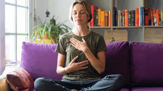 Woman practicing self-compassion with hand on heart in mindful meditation at home