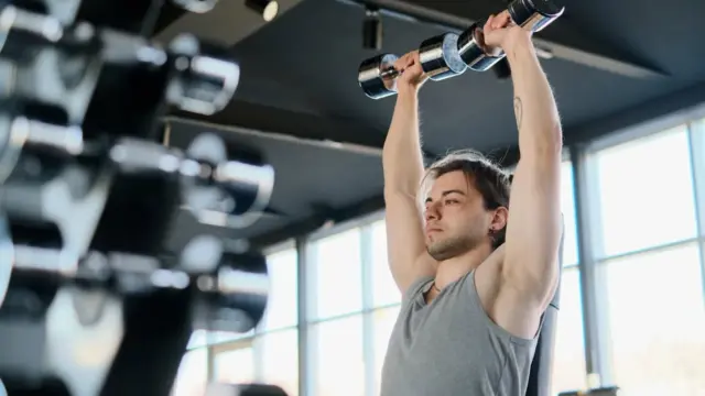 Man performing dumbbell shoulder press in gym representing safe shoulder training alternatives