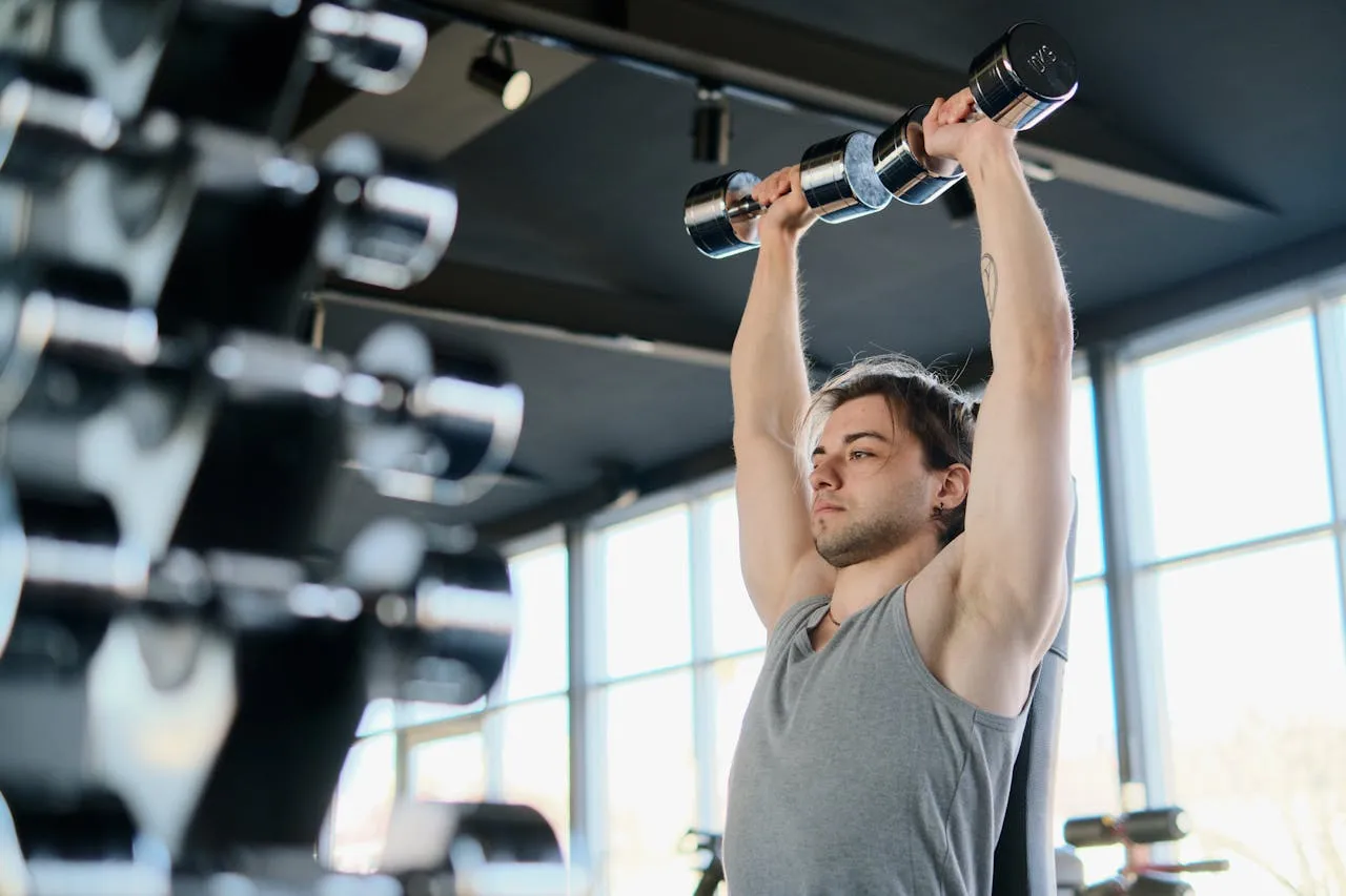 Man performing dumbbell shoulder press in gym representing safe shoulder training alternatives