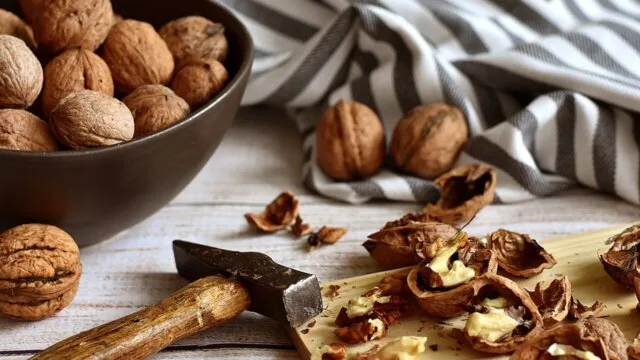 Whole walnuts in a bowl and cracked walnuts on a wooden board showing the health benefits of whole nuts for longevity