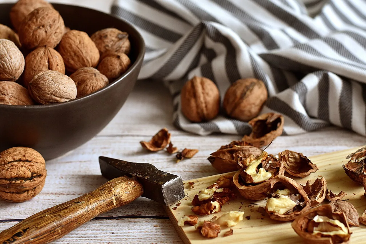 Whole walnuts in a bowl and cracked walnuts on a wooden board showing the health benefits of whole nuts for longevity