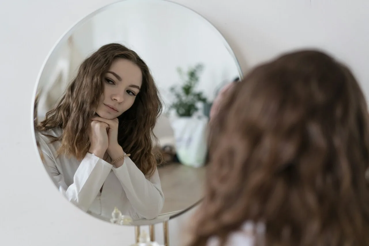 Young woman looking at herself in a round mirror practicing self-awareness to overcome people-pleasing