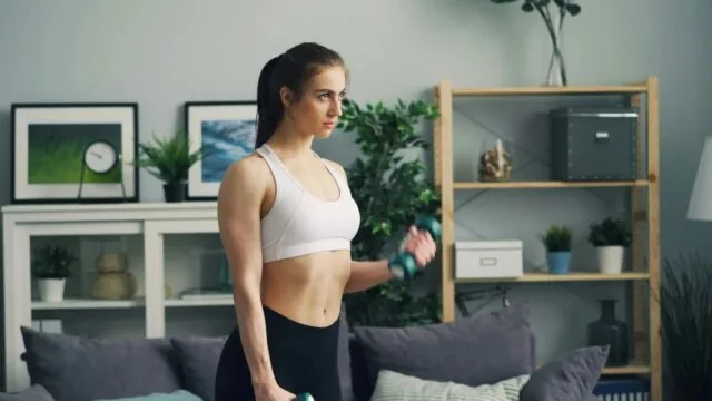 Woman doing strength training with dumbbells at home living room fitness workout