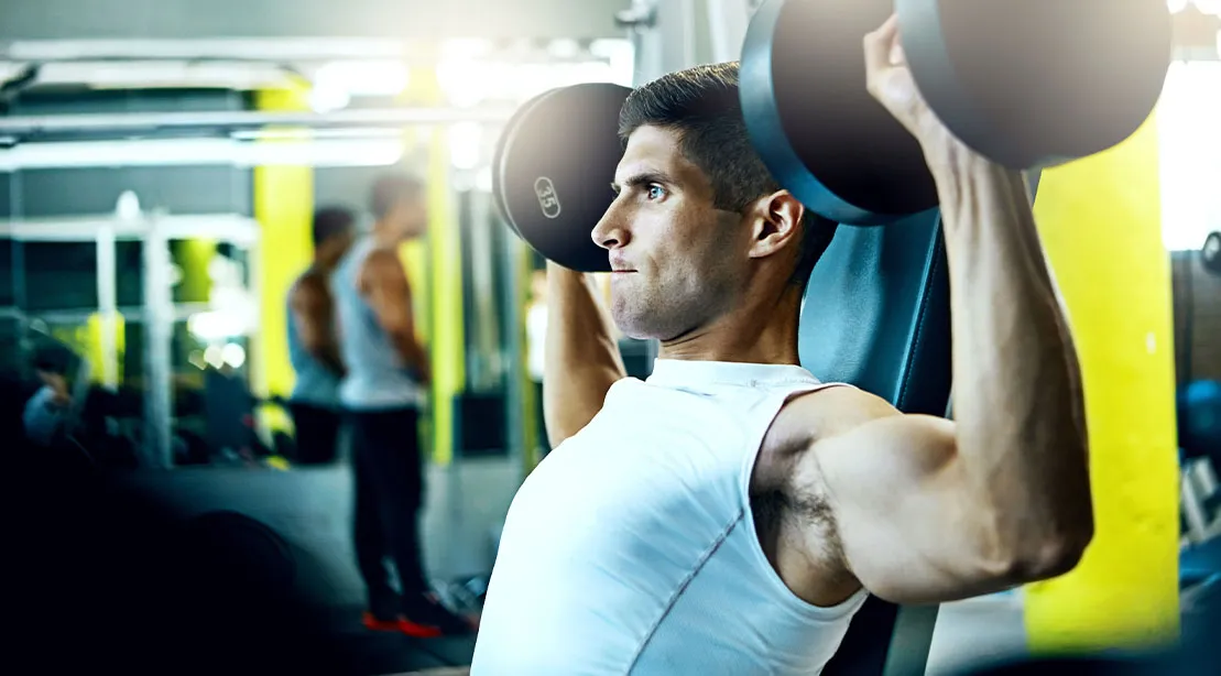 Young man performing seated dumbbell shoulder press exercise in gym to build next-level deltoids