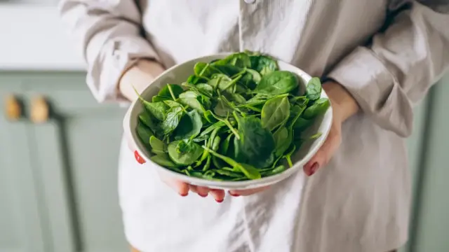 Woman holding a bowl of fresh spinach leaves as one of the best magnesium-rich dark leafy greens for supporting energy, muscle function and sleep health