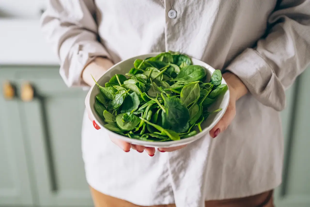 Woman holding a bowl of fresh spinach leaves as one of the best magnesium-rich dark leafy greens for supporting energy, muscle function and sleep health
