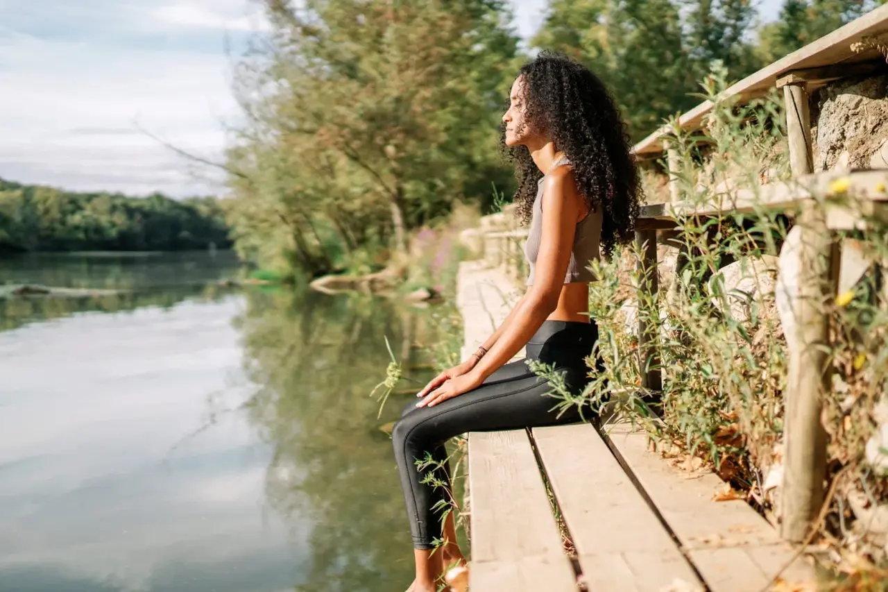 Woman sitting calmly by a river practicing mindful breathing to support emotional regulation