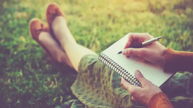 Woman journaling outdoors on grass to calm overthinking and clear her mind