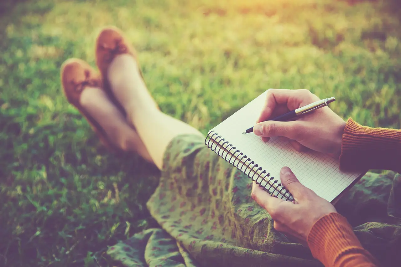 Woman journaling outdoors on grass to calm overthinking and clear her mind