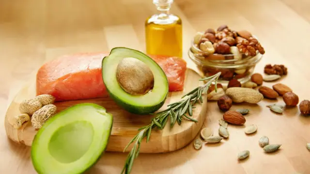 Healthy dietary fats including avocado, salmon, mixed nuts and olive oil arranged on a wooden board