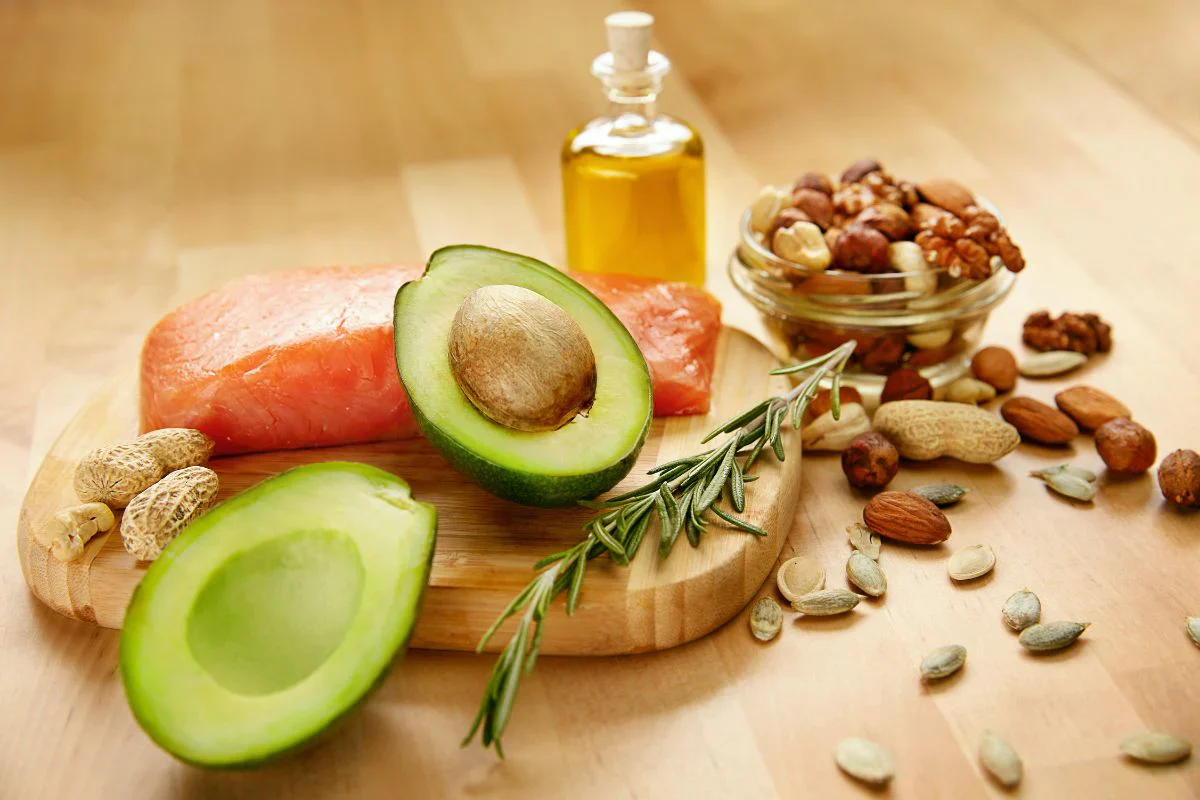 Healthy dietary fats including avocado, salmon, mixed nuts and olive oil arranged on a wooden board
