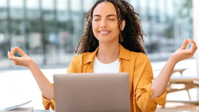 Young female student practicing mindfulness meditation at desk with laptop to relieve school stress