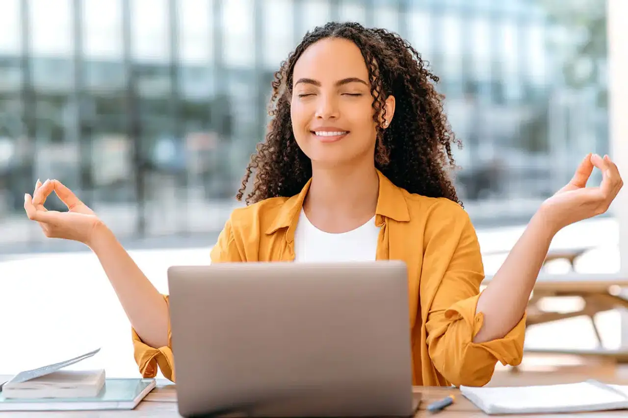 Young female student practicing mindfulness meditation at desk with laptop to relieve school stress