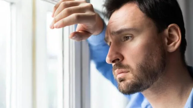 Man gazing thoughtfully out a window representing emotional suppression and the hidden cost of saying I'm fine
